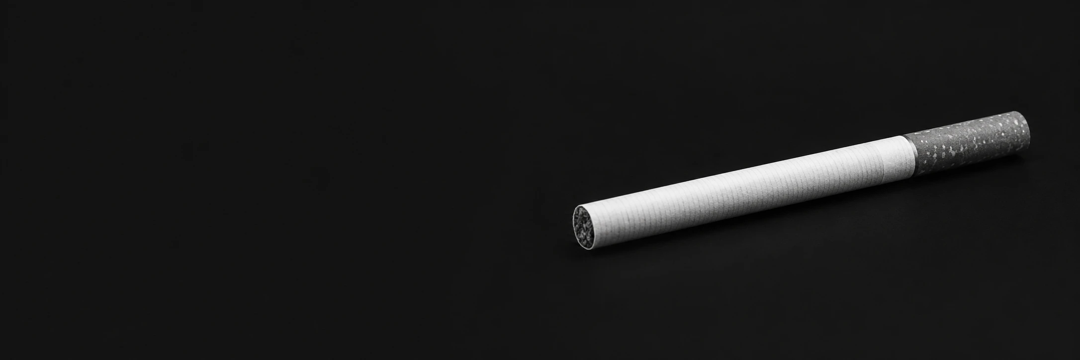 A single unlit cigarette in black and white on a dark background